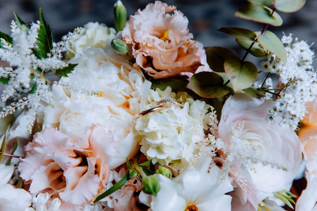 Alliances mariage et bouquet floral pivoines pastel Deux alliances en or (une pavée diamants) reposent sur un luxueux bouquet de mariage: pivoines blanches, fleurs pêche et eucalyptus.
